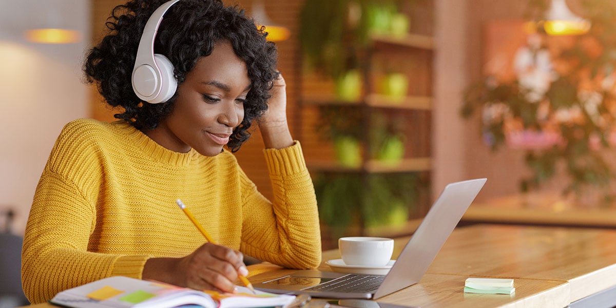 A woman in a yellow shirt with headphones studying real estate investing on a laptop