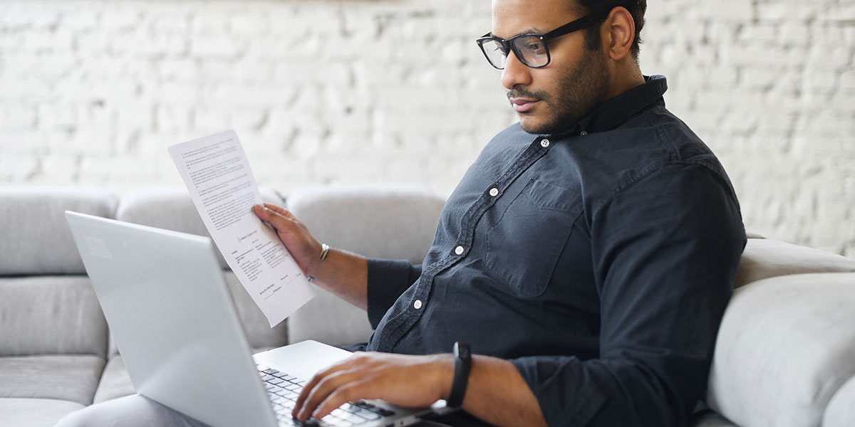 A man in a dark shirt finding deals looking over paperwork on a couch