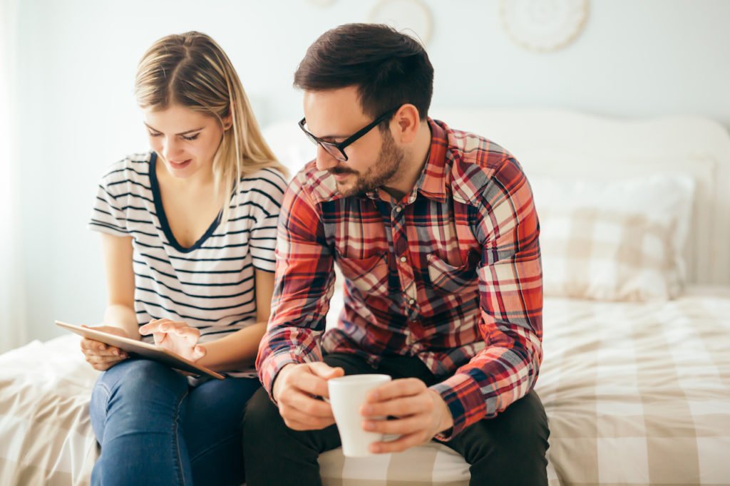 A couple looking over a checklist on a bed with coffee.