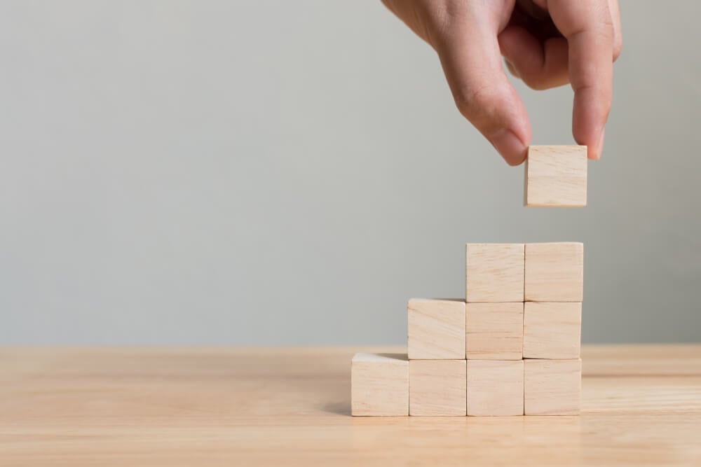 A person building a small staircase of wooden cubed blocks.