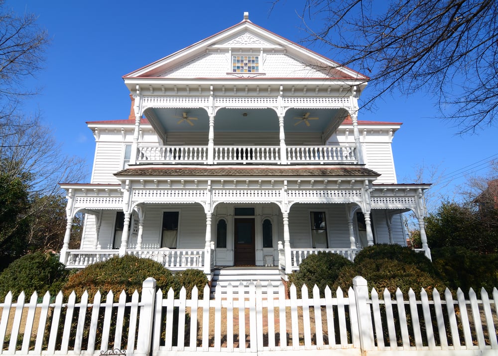 A white Victorian house with a white picket fence ready for a fix and flip.