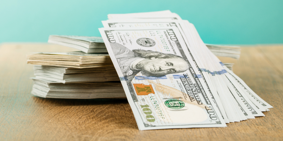 a pile of $100 bills on a table with a seafoam colored wall in the background