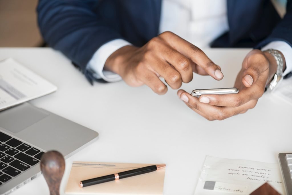 A man working on his phone at his desk of a papers and a laptop.