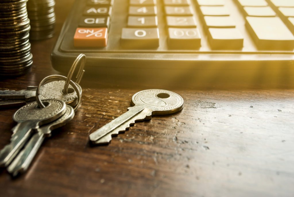 A closeup of keys to a fix and flip property on a desk next to a calculator.