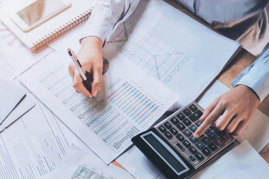 A person looking at a spreadsheet and working on a calculator.