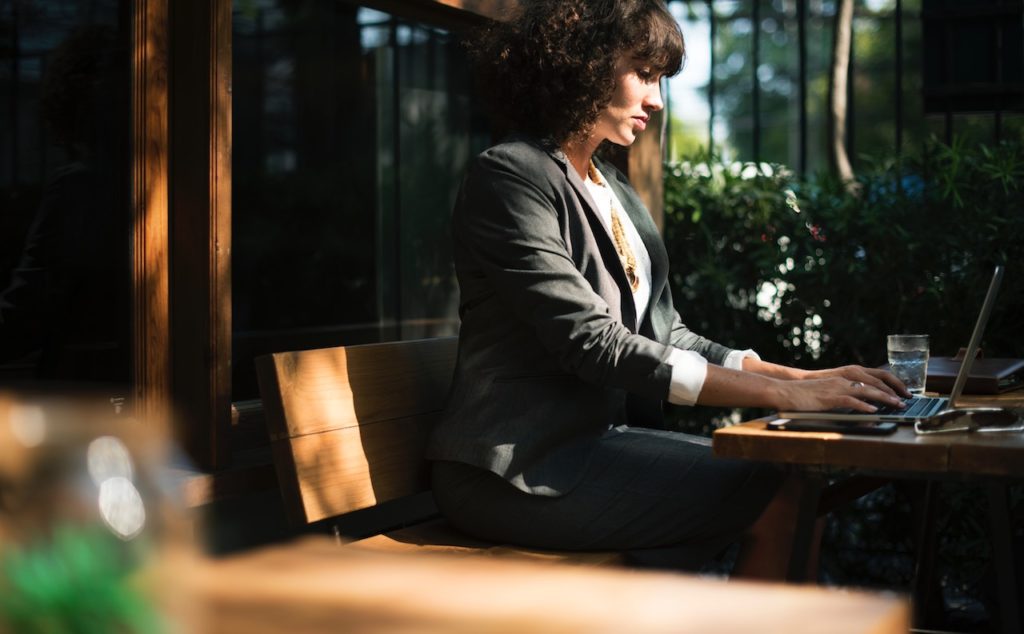 A sharply dressed young woman in an office concentrating on a fix and flip plan on her computer.