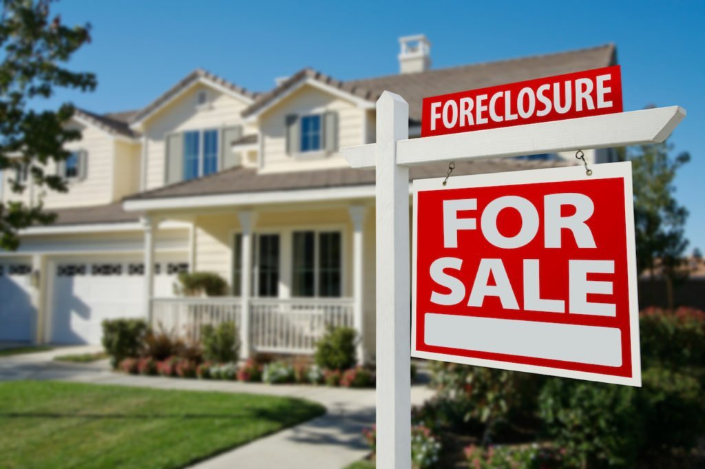 A foreclosure sign in front of a large, beautiful white home.