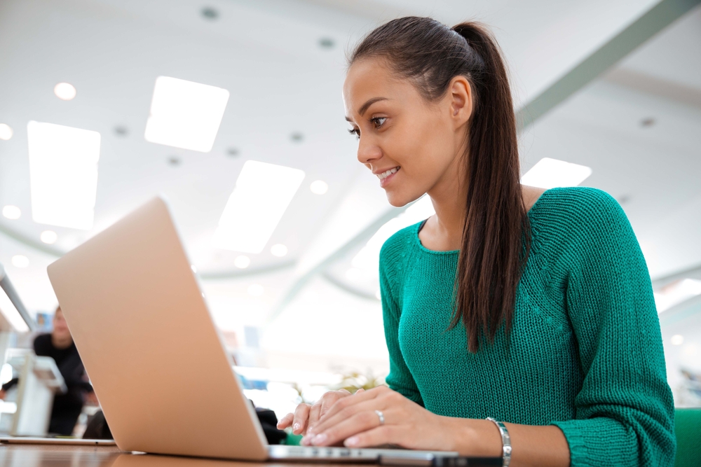 A woman in a green shirt smiling and looking sat a laptop.