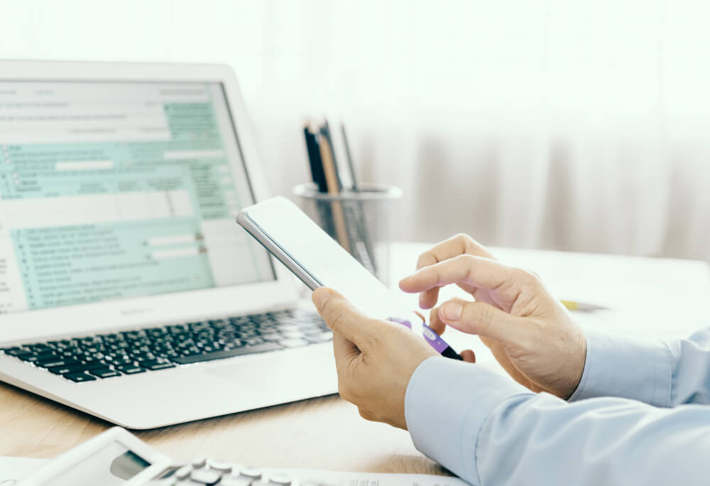 A man working on a tablet at a desk in front of a laptop.