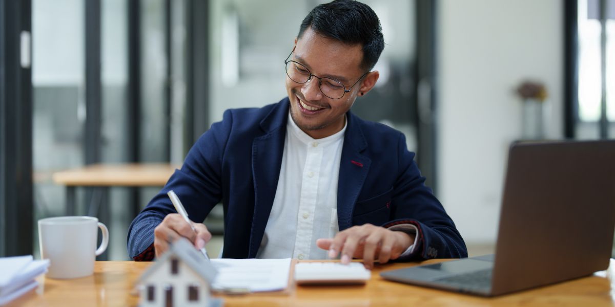 Real estate investor calculating finances and assessing property value on a laptop with a miniature house model on the desk.