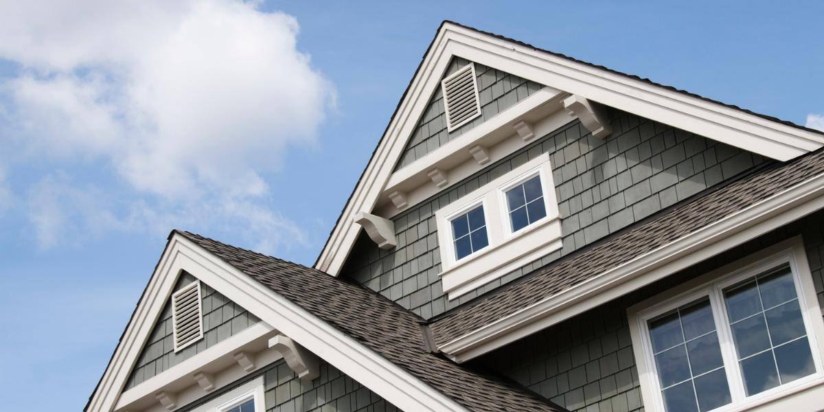 A close-up view of a single-family rental house with gray siding and white trim under a clear blue sky.