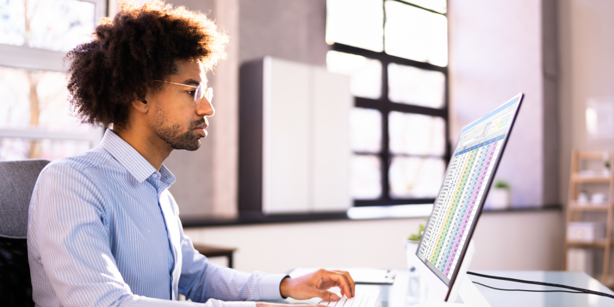 A focused young male real estate investor analyzing real estate data on his computer in a bright, modern office.