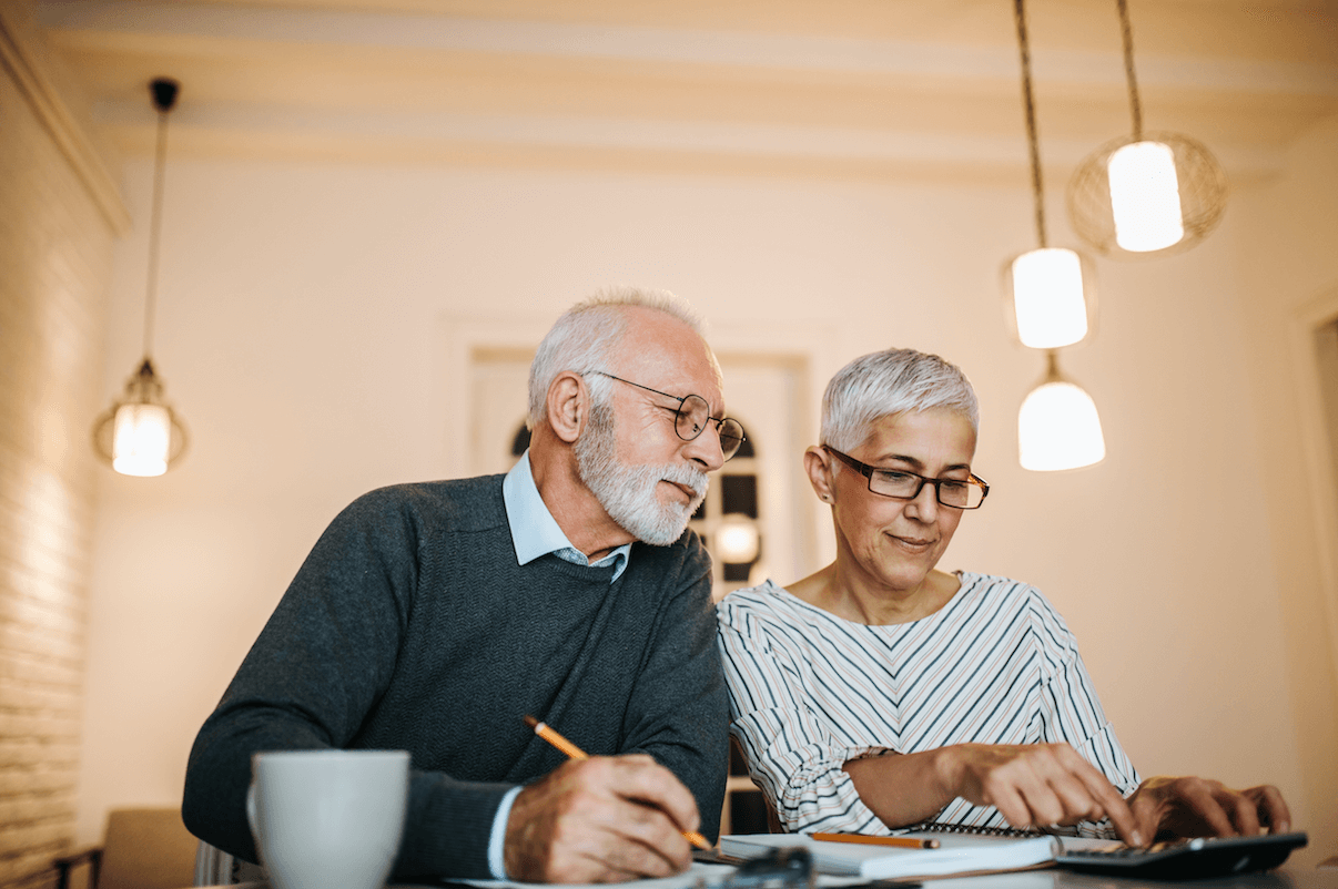 An elderly couple in their home looking at paperwork and making lists with coffee.